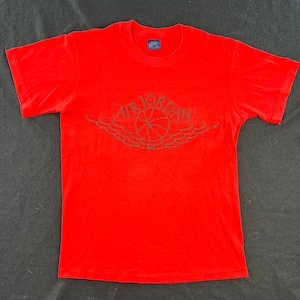 May include: Red t-shirt with a black and white Air Jordan logo. The logo features a basketball and wings.