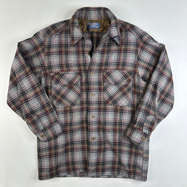 May include: A brown, white, and red plaid flannel shirt with a button-up front and two chest pockets.
