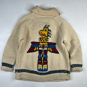 May include: A cream-colored knitted cardigan with a colorful Native American totem pole design on the front. The cardigan has a fold-over collar and a blue and yellow trim around the bottom and cuffs.
