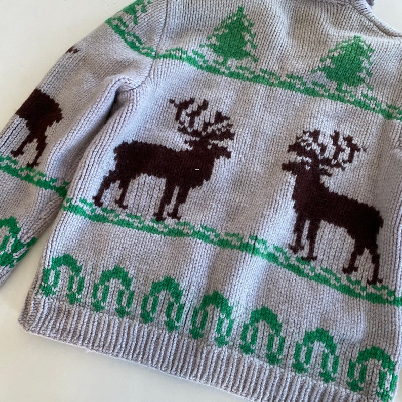 May include: A gray knitted sweater with a green and brown reindeer pattern. The sweater has a high neck and long sleeves.