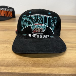 以下が含まれることがあります： National Basketball Association、Grizzlies、Vancouverと刺繍された黒い野球帽。フロントパネルには、Grizzliesという文字とクマのグラフィックが描かれており、すべてティール、白、赤の糸で縫い付けられています。