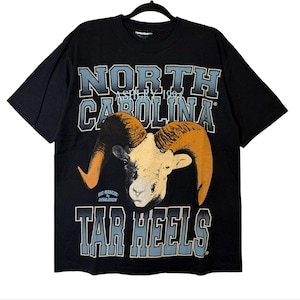 May include: Black t-shirt with a ram graphic and the text "NORTH CAROLINA" and "TAR HEELS". The ram has tan horns and a cream-colored face. The text is in a light blue and white colour scheme.