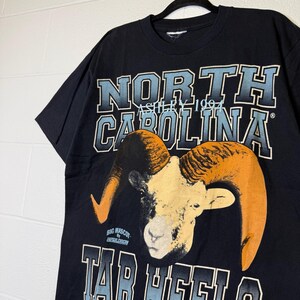 May include: Black t-shirt with a ram graphic, orange horns, and the text "NORTH CAROLINA" in blue and white. The shirt also features "TAR HEELS" and "ASHLEY 1994".
