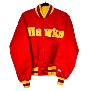 Könnte beinhalten: Rote Satin-Bomberjacke mit gelben und roten Streifen an Ärmelbündchen und Kragen. Die Jacke hat einen Knopfverschluss und trägt den Schriftzug "Hawks" in gelben Stickbuchstaben auf der Vorderseite.