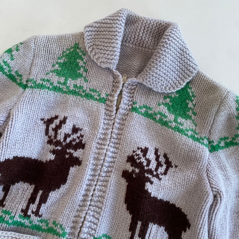 May include: A gray knitted cardigan with a zipper closure and a brown and green reindeer pattern.