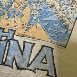 Puede incluir: Camiseta de color crema con un estampado gr&aacute;fico que presenta una banda de m&uacute;sica en uniformes azules y la palabra "Havana" en letras azules grandes. El dise&ntilde;o incluye el texto "&copy; JOHN HOLLADAY" y "GRAM MARKETING &copy; Holladay Prints, Inc."