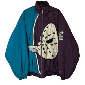 May include: A teal, purple, and white Mighty Ducks hockey jacket. The jacket has a full zip, a large hockey mask graphic, and the team logo. The jacket is made of a lightweight material and has a high collar.