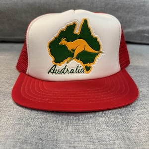 Peut inclure: Casquette de camionneur rouge et blanche avec un dos en filet rouge. Le panneau avant présente un contour vert de l'Australie, un kangourou et le mot "Australia" en vert.