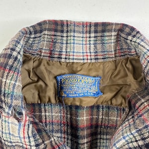 May include: A brown, blue, and white plaid flannel shirt with a blue label that reads "WARRANTED TO BE A PENDLETON" and "PURE VIRGIN WOOL MADE IN U.S.A."