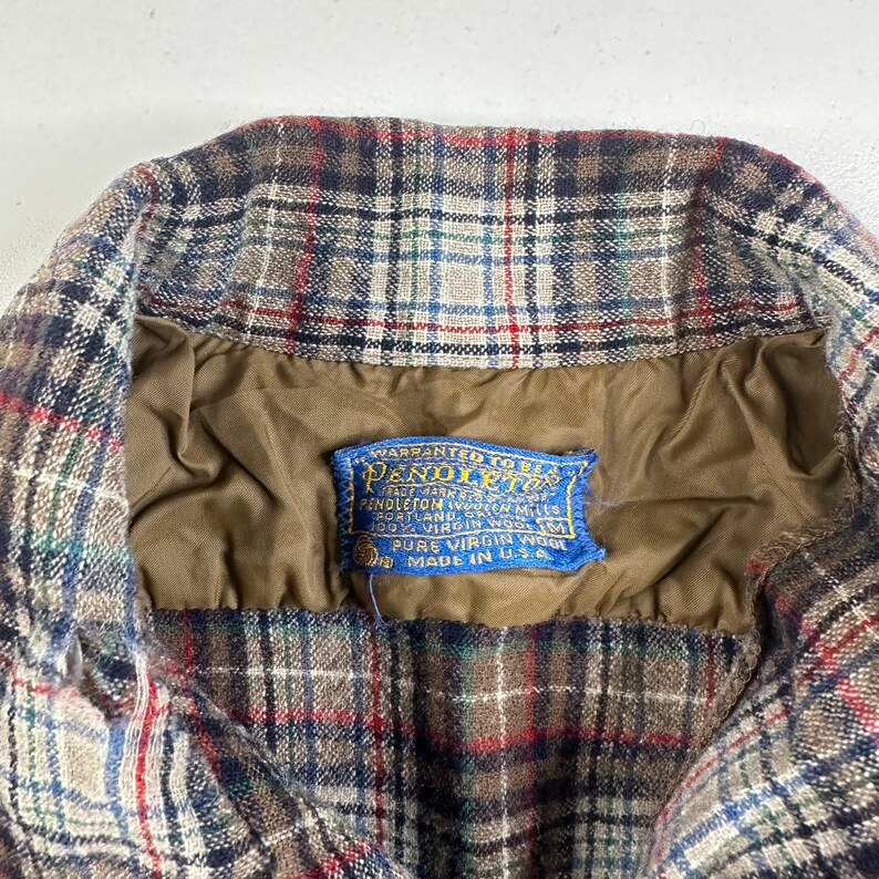 May include: A brown, blue, and white plaid flannel shirt with a blue label that reads "WARRANTED TO BE A PENDLETON" and "PURE VIRGIN WOOL MADE IN U.S.A."