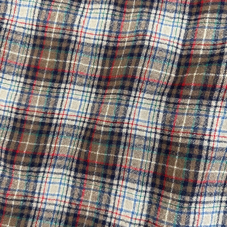 May include: A close-up of a brown, white, blue, and red plaid fabric. The fabric has a woven texture and is made of a soft, comfortable material.