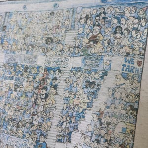 Puede incluir: Una camiseta gris claro con una ilustraci&oacute;n detallada de una multitud en un estadio. La obra de arte incluye numerosas figuras en azul y blanco, con pancartas y el texto "UNC Champions" y "We Tar Heels".