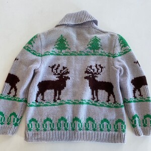 May include: A gray knitted cardigan with a brown and green reindeer pattern. The cardigan has a collared neckline and a button closure.