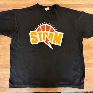 May include: Black t-shirt featuring a graphic of a basketball with the text "Saskatchewan Storm" in orange and white.