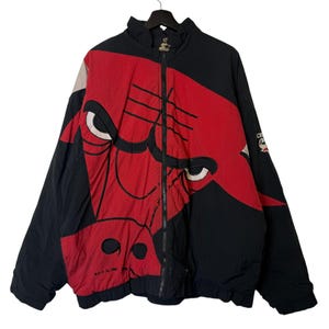Puede incluir: Chaqueta Starter de los Chicago Bulls en negro y rojo con cierre de cremallera completo. La chaqueta presenta un gran logotipo de toro en la parte delantera y el logotipo del equipo en la manga. Fabricada en material ligero.