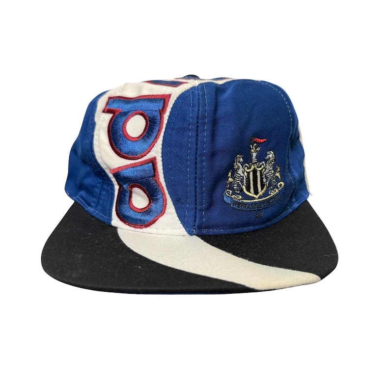 May include: A blue, white, and black baseball cap with the letters "NU" in red and white. The cap features a team crest on the side and a black brim. The hat is a vintage style.