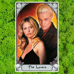May include: A tarot card featuring two people, a woman with blonde hair and a man with blonde hair, against a red and yellow background. The card is framed with a white border and the words "The Lovers" at the bottom. The background is green.