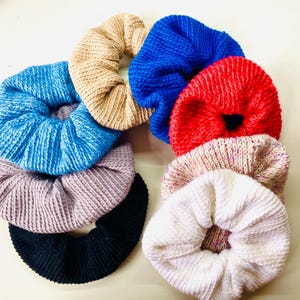 Puede incluir: Un conjunto de 8 scrunchies de pelo de punto de colores variados, incluyendo azul, rosa, blanco, gris y negro.