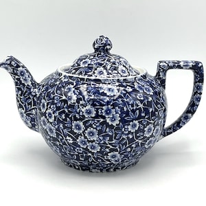 Könnte beinhalten: Eine Keramik-Teekanne mit einem dunkelblauen und weißen Blumenmuster, das die gesamte Außenseite einschließlich Deckel, Ausguss und Griff bedeckt. Das Design besteht aus kleinen, detaillierten Blüten und Blättern mit einem passenden Deckel.