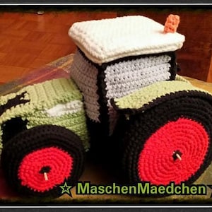 Peut inclure: Un tracteur jouet en crochet avec des détails verts, noirs et rouges. Le tracteur a un toit blanc et une roue noire et rouge.