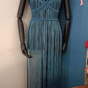 Może przedstawiać: Turkusowy top halterowy z makramą i frędzlami. Top ma otwór w kształcie dziurki od klucza z przodu i jest ozdobiony złotymi koralikami.