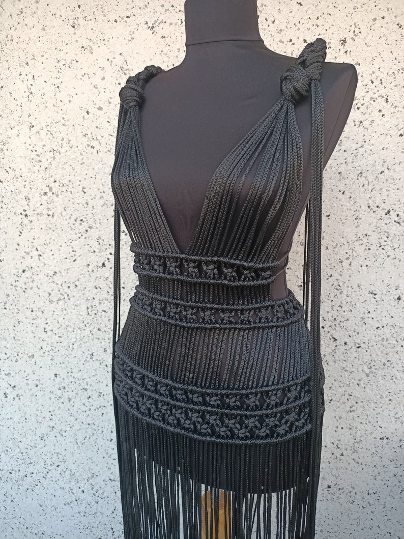 May include: A black crocheted dress with a deep V-neckline and fringe detailing. The dress is made of thick rope and has a fitted bodice and a flowing skirt.