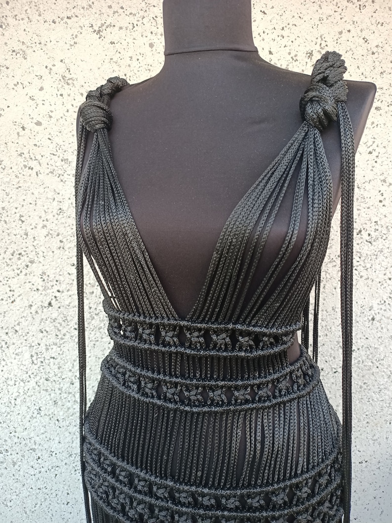 May include: A black halter dress crafted entirely from knotted rope. The dress features a deep V-neckline and a fitted bodice. The skirt is made up of a series of horizontal rows of knots.