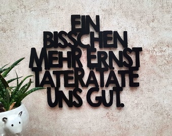 May include: Black wall decor with the words "Ein bisschen mehr Ernst laterate uns gut".