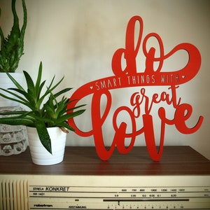 May include: Red wooden sign with the text "Do smart things with great love" in a decorative font. The sign is on a wooden surface with a radio below it.
