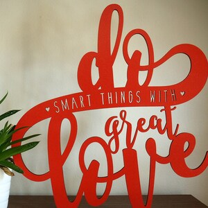 May include: Red wooden sign with the words "Do Smart Things With Great Love" in a cursive font.