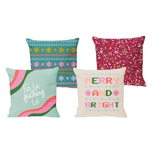 May include: Four decorative throw pillows with different Christmas-themed designs. One pillow features a teal and pink geometric pattern, another has a red background with confetti, a third has a green and pink "Merry and Bright" design, and the last one has a teal background with the phrase "Fa La Fucking La" in pink and green.