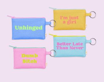 May include: Four small, rectangular zippered pouches in pastel colors: blue, yellow, pink, and light blue. Each pouch has a different phrase printed on it: "Unhinged", "I'm just a girl", "Dumb Bitch", and "Better Late Than Never". Each has a small metal ring.