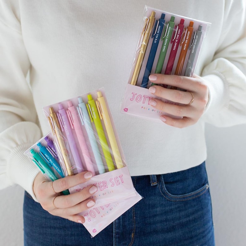May include: Two sets of colorful pens with motivational phrases. The first set is a pack of six pastel pens with the phrase "The Power Set" and the second set is a pack of six metallic pens with the phrase "Jot It Down" and the text "Pack of Six".