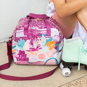 May include: A pink and white patterned tote bag with a burgundy strap and the text "Do the thing". The bag is sitting on a concrete surface next to a pair of mint green roller skates.