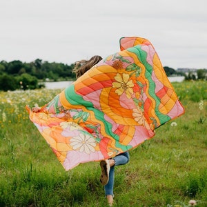 girl running in field of flowers holding a blanket behind her with big flowers and rainbow swirls.