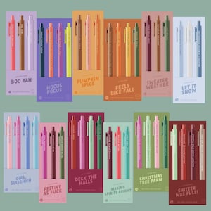 May include: A collection of twelve sets of three retractable gel pens, each set featuring a unique color palette and themed text printed on the barrels. The sets include phrases like Boo Yah, Hocus Pocus, Pumpkin Spice, Feels Like Fall, Sweater Weather, Let It Snow, Girl Sleighhh, Festive As Fuck, Deck The Halls, Making Spirits Bright, Christmas Tree Farm, and Shitter Was Full.