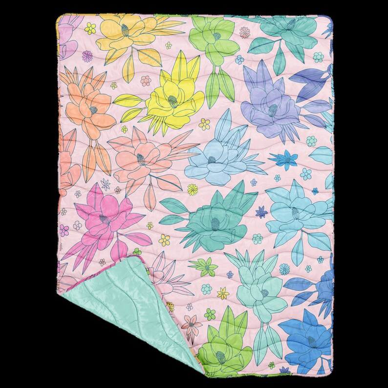 A multicolored, quilted floral puffy blanket with a solid light blue back side. Flowers are varying in shape and size.