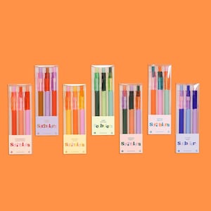 May include: Seven clear plastic boxes of colorful pens on an orange background. Each box contains multiple pens in various colors, with labels such as "Strawberry Shortcake" and "Cloud Nine". The pens are arranged in a neat row.