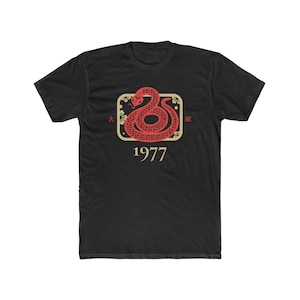 Può includere: T-shirt nero con una grafica di un serpente rosso e oro con il testo "火蛇" e "1977".
