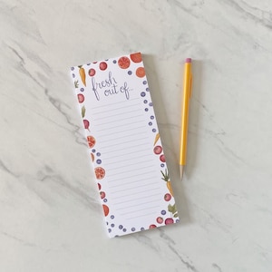 May include: A rectangular notepad with the words "fresh out of..." in script. The notepad is decorated with watercolor illustrations of fruits and vegetables. A yellow pencil with a pink eraser rests beside the notepad.
