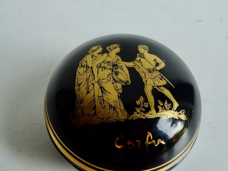 May include: A black and gold ceramic trinket box with a Greek mythological scene and the word "Corfu" inscribed on the bottom.