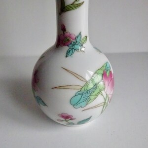 May include: A white ceramic vase with a round body and a narrow neck. The vase is decorated with a floral pattern in shades of pink, blue, green, and gold.