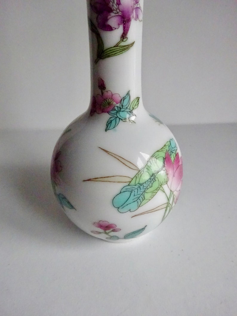 May include: A white ceramic vase with a round body and a narrow neck. The vase is decorated with a floral pattern in shades of pink, blue, green, and gold.