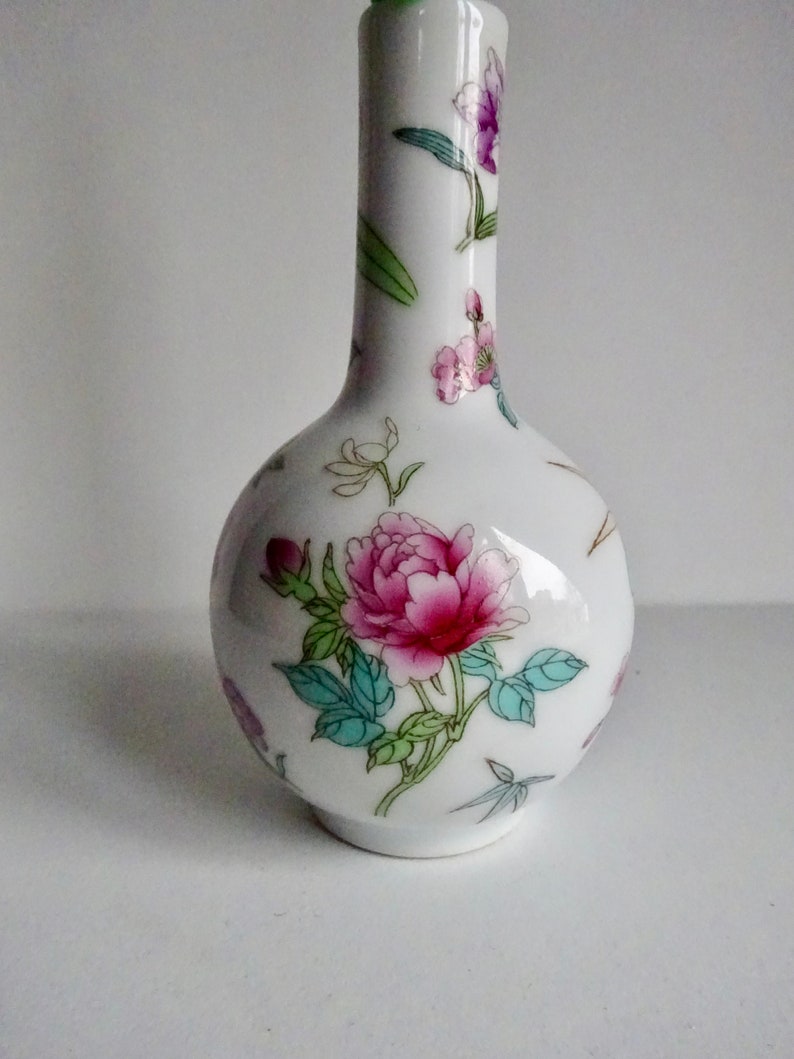 May include: A white porcelain vase with a floral design. The vase has a round body and a long, slender neck. The flowers are pink, green, and white.