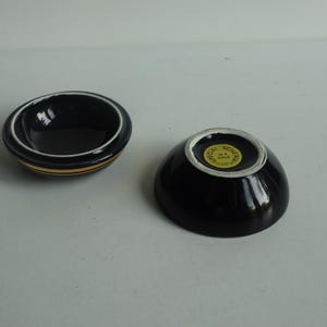 May include: Two small black ceramic bowls with gold trim. The bowl on the right has a gold sticker on the bottom that reads "Special Souvenir Hong Kong".