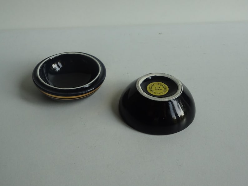 May include: Two small black ceramic bowls with gold trim. The bowl on the right has a gold sticker on the bottom that reads "Special Souvenir Hong Kong".