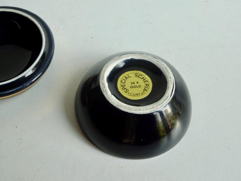 May include: A black ceramic bowl with a gold rim and a gold sticker on the bottom that reads "Special Scheria 24 K Gold Corfu".