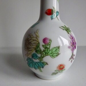 May include: A white porcelain vase with a narrow neck and a round body. The vase is decorated with a floral pattern in shades of pink, purple, green, yellow, and red.