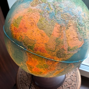 Op de afbeelding: Een bolvormige verlichte wereldbol met een gedetailleerde politieke kaart van Afrika, Europa en het Midden-Oosten. Het oppervlak toont diverse landen in tinten oranje, groen en geel, met zwarte tekstlabels voor steden, regio's en wateren.