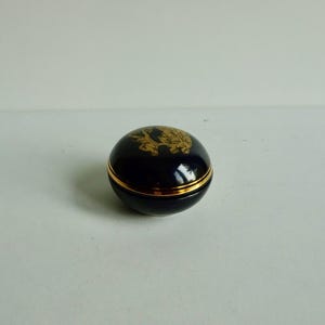 May include: A small, round, blue and gold trinket box with a gold design on the lid.